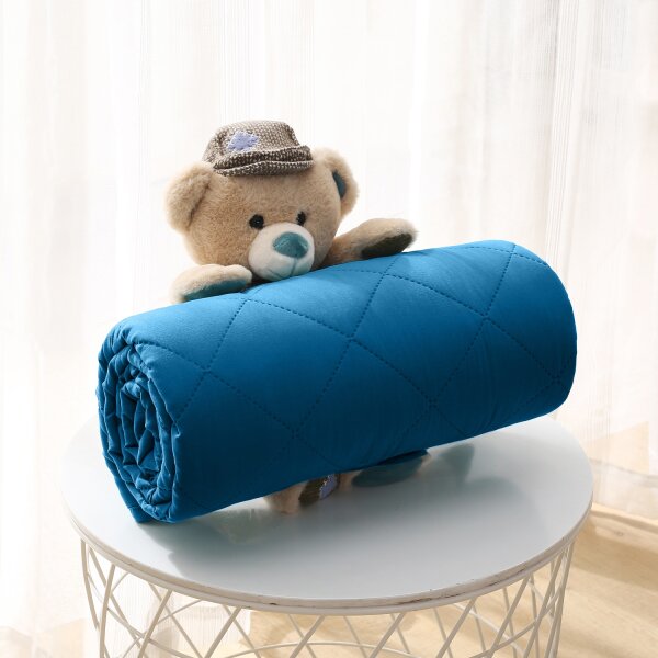 Teddybär hält eine zusammengerollte blaue Steppdecke in seinen Armen
